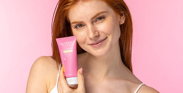 A woman holding a pink tube of face cream.