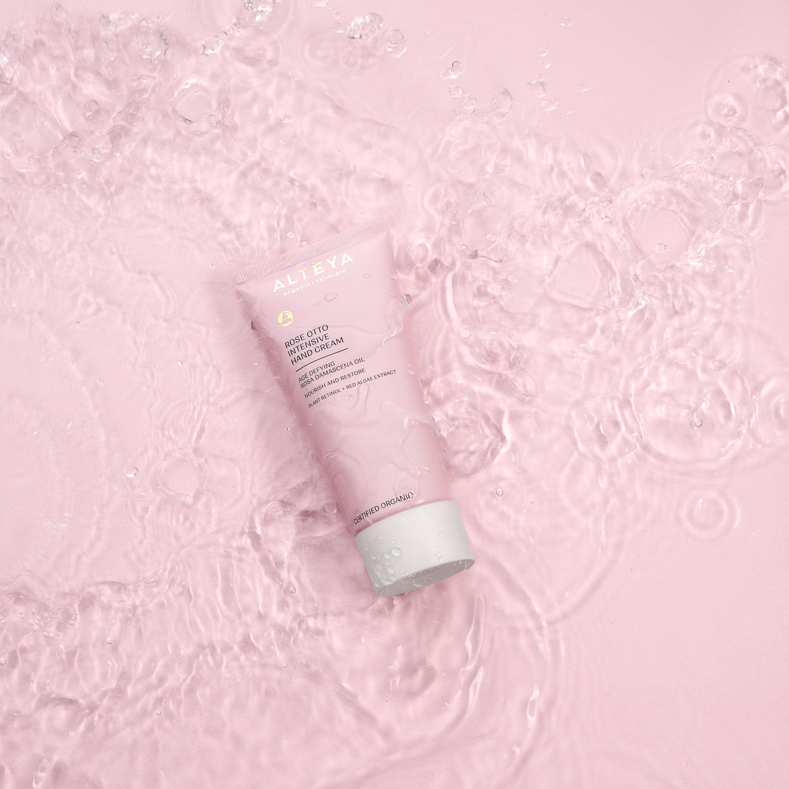 A pink tube of Alteya Organics Organic Rose Otto Intensive Hand Cream, sitting on top of a pink background.