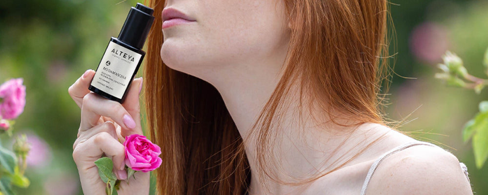 A woman with red hair is smelling a rose.
