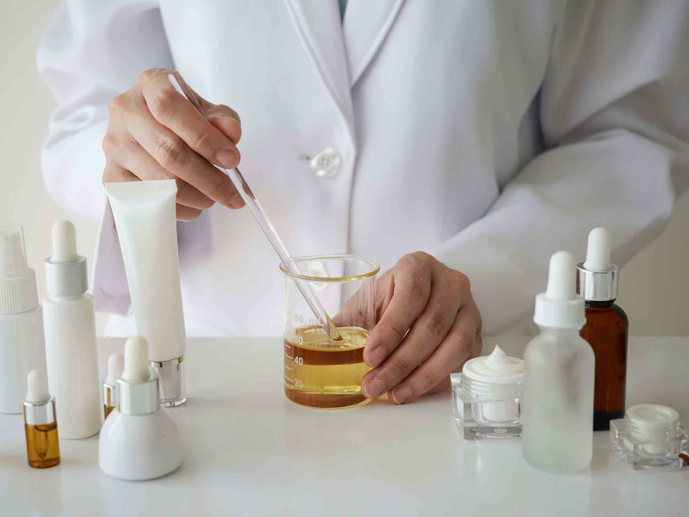 A woman in a lab coat is pouring liquid into a glass.