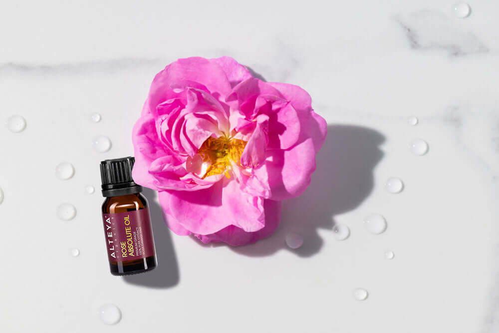 A bottle of rose essential oil next to a pink flower.