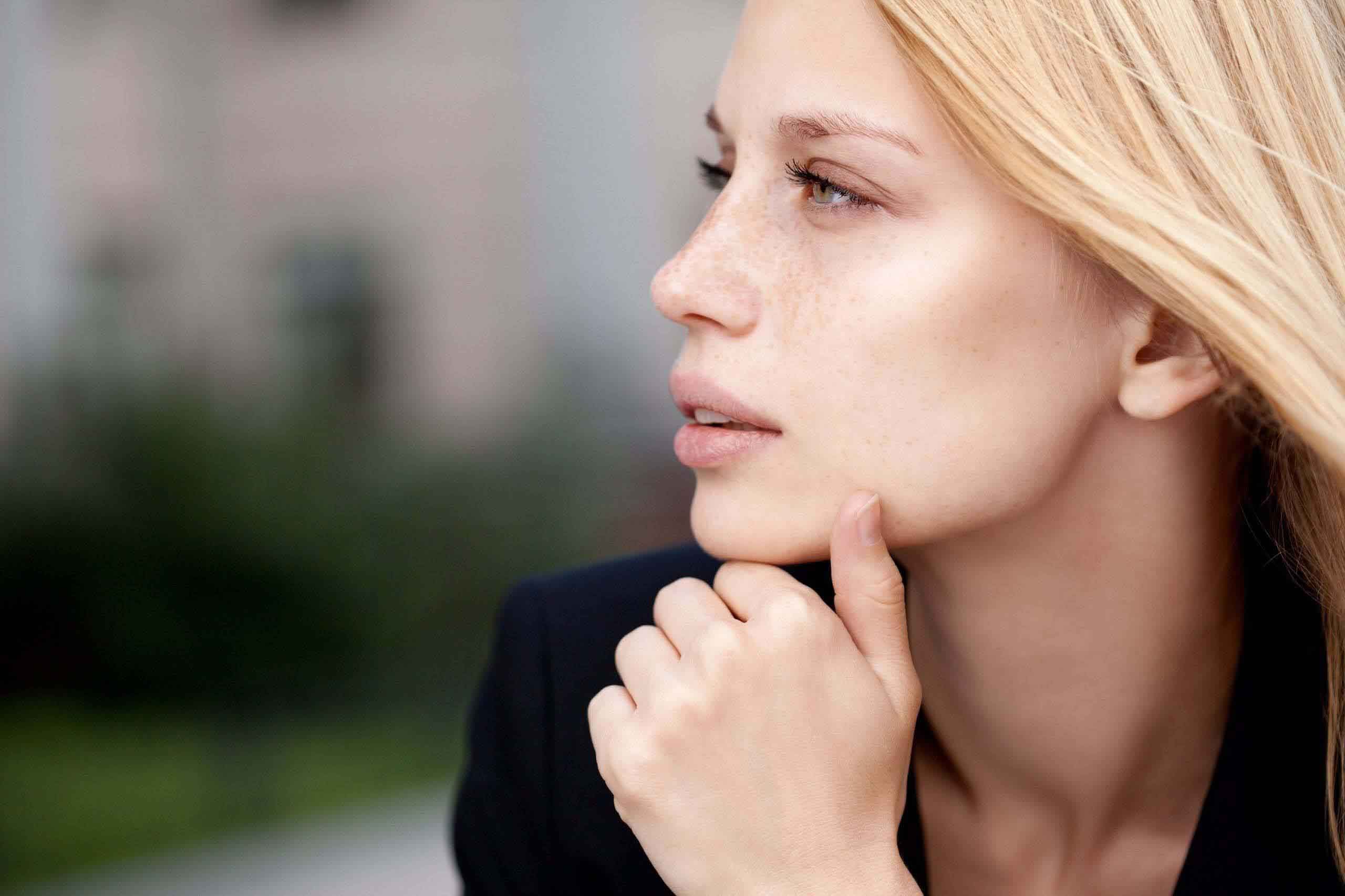 A blond woman in a business suit looking at her chin.