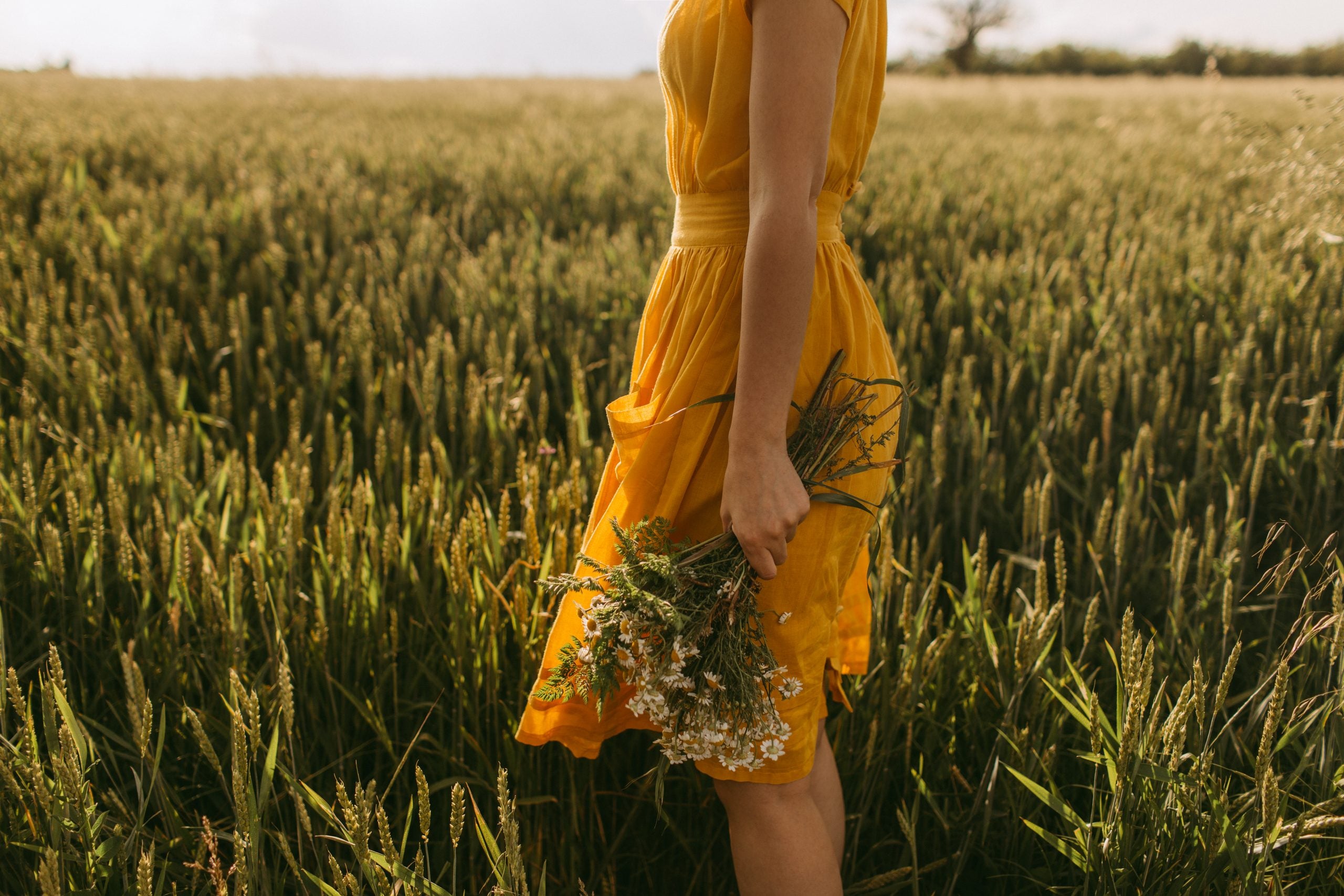 A woman in a yellow dress standing in a wheat field.