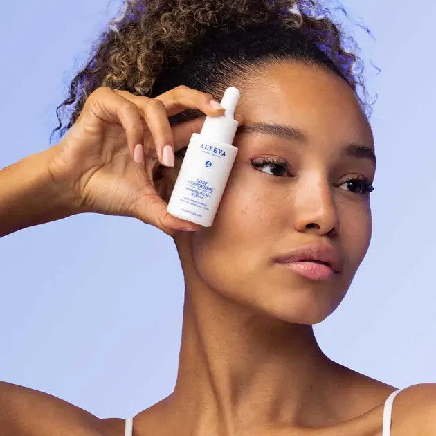 A woman holding a bottle of serum on her face.