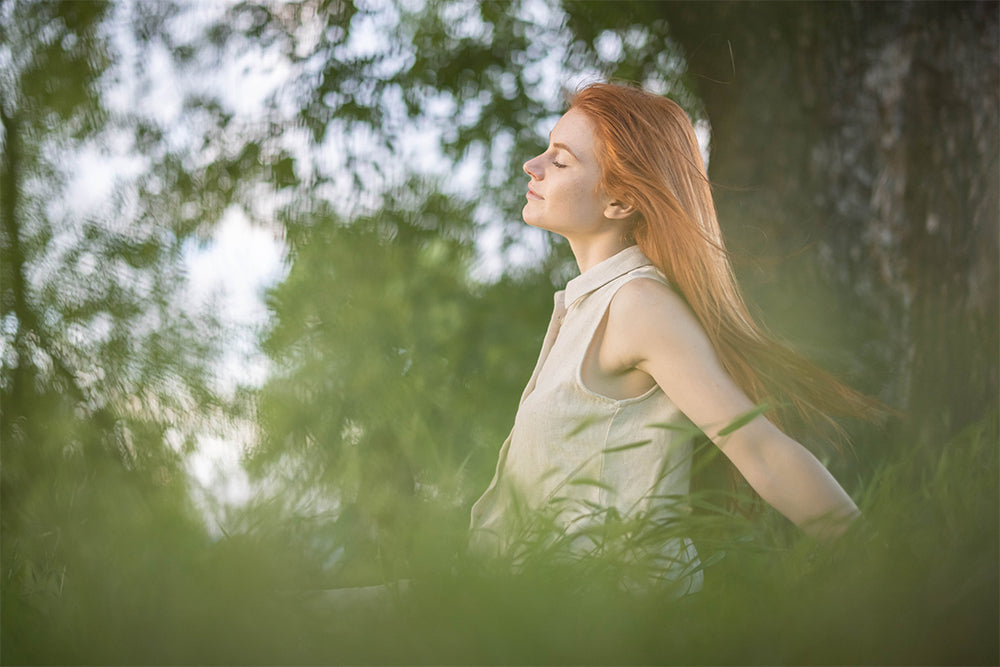 A red haired woman is sitting in the grass under a tree.