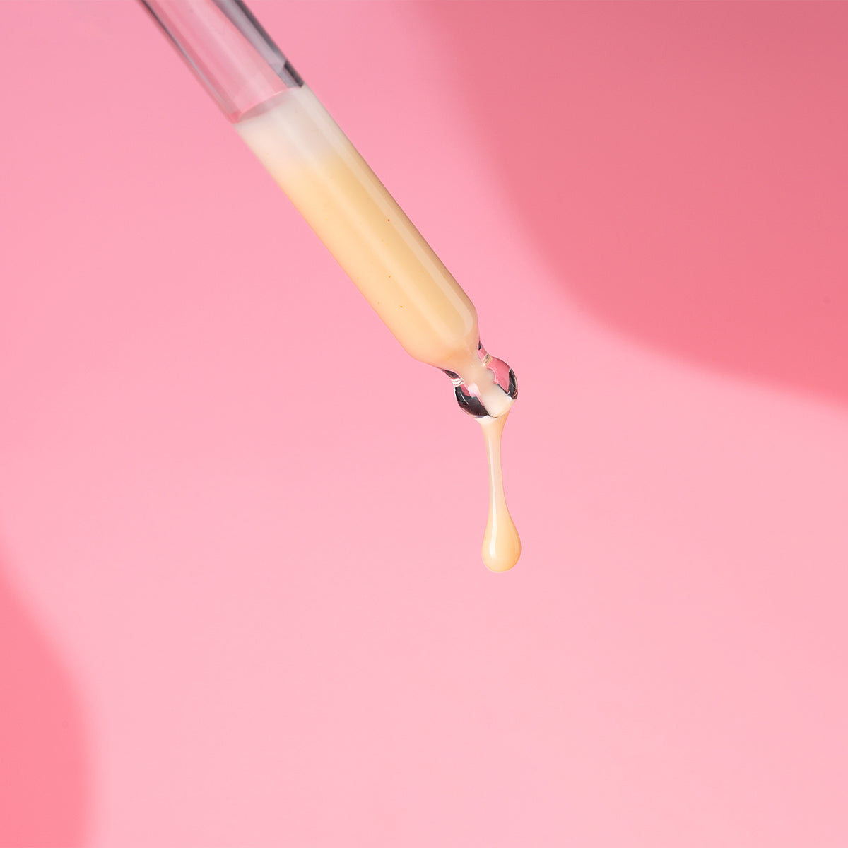 A person is pouring the Alteya Organics Bio Damascena Rose Otto Regenerating Concentrate into a tube on a pink background.