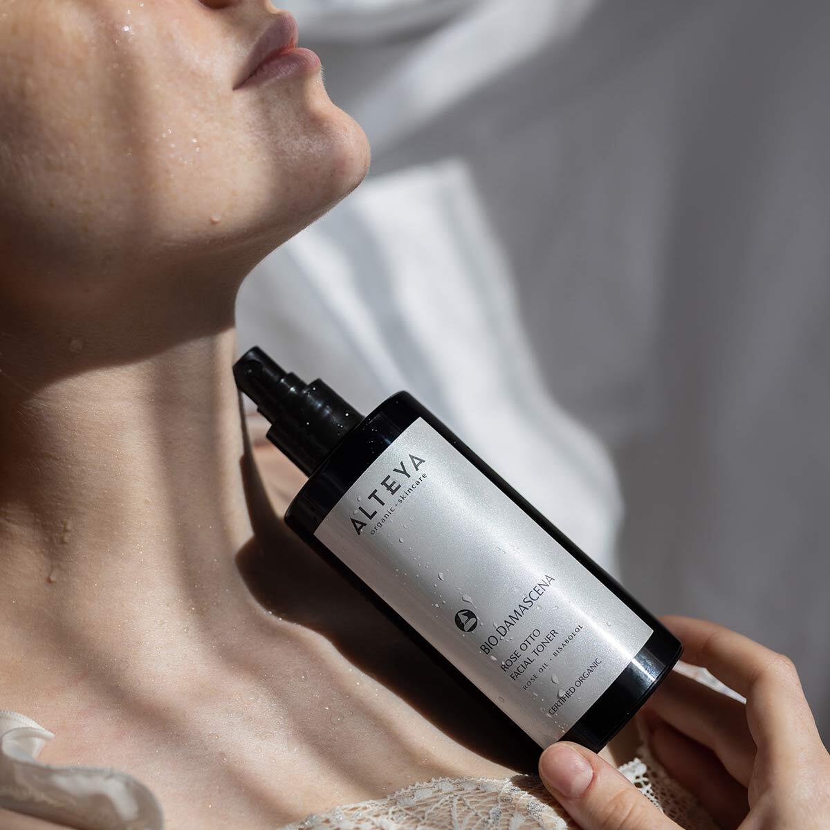 A woman holding a bottle of Alteya Organics Bio Damascena Rose Otto Facial Toner, which clarifies and hydrates.