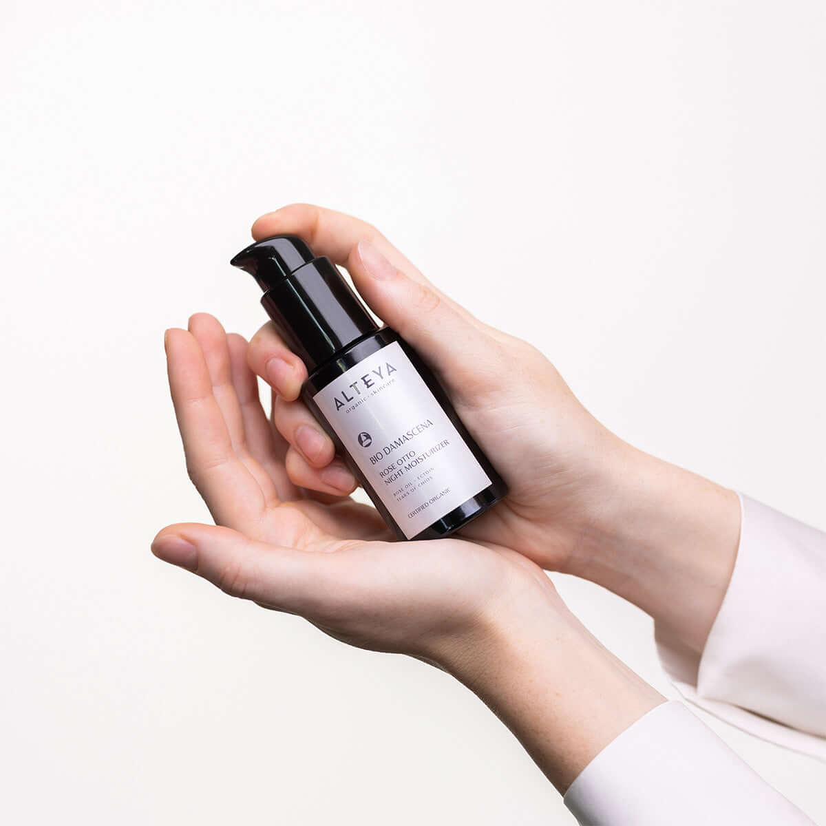 A woman's hand holding a bottle of Alteya Organics Bio Damascena Rose Otto Night Moisturizer.