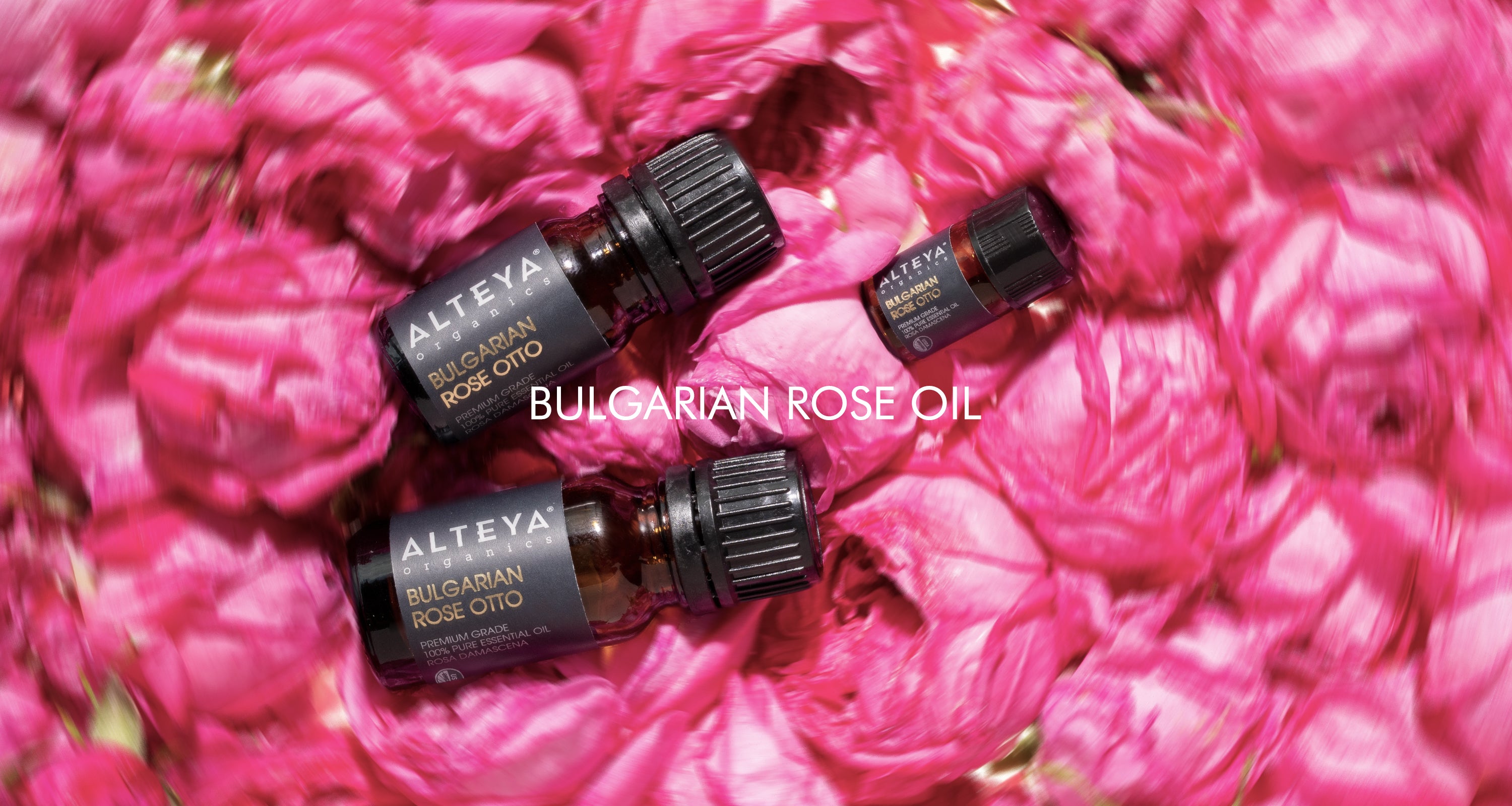 Two bottles of essential oils surrounded by pink flowers.