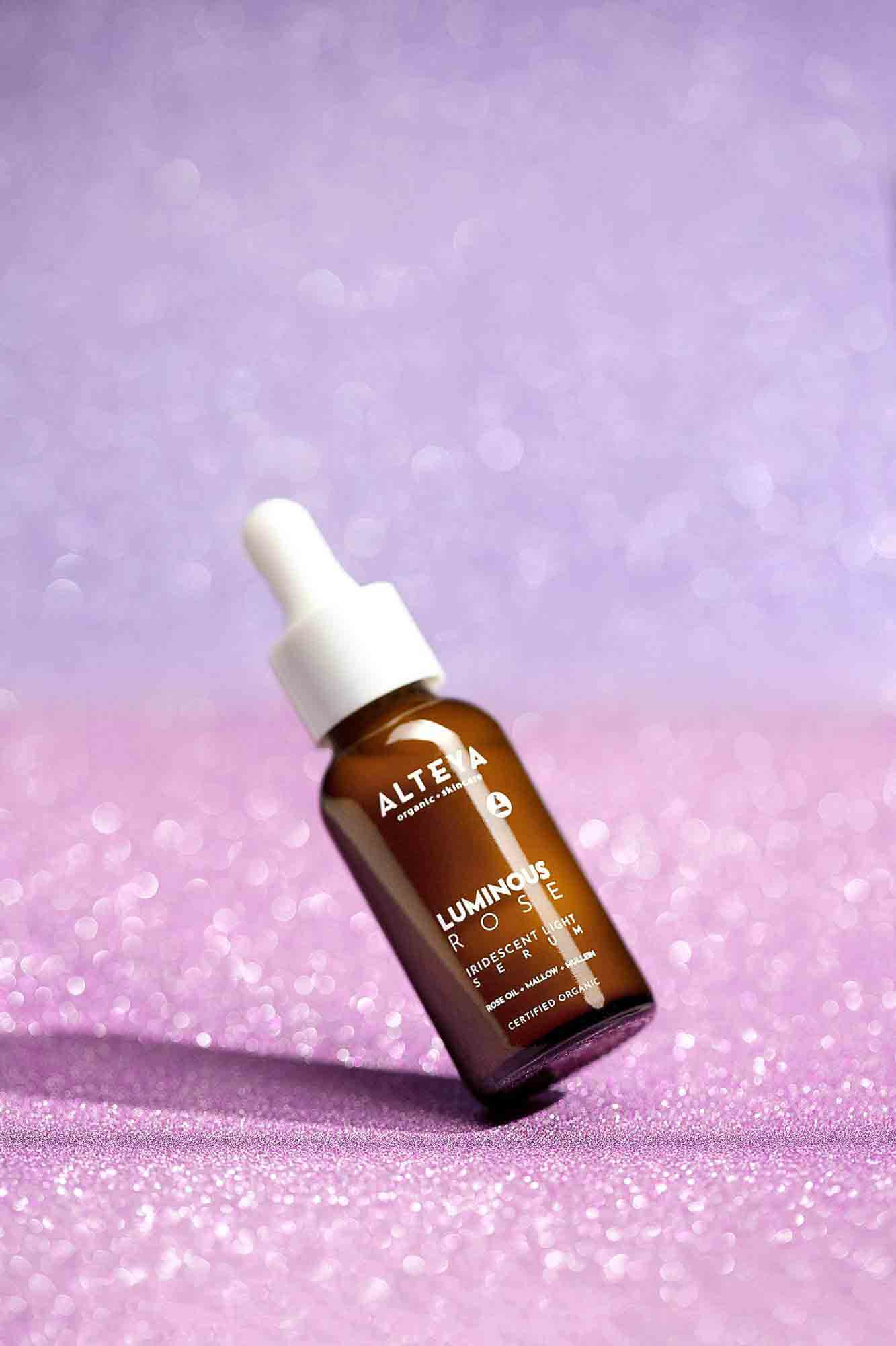 A bottle of Luminous rose serum on a purple background.