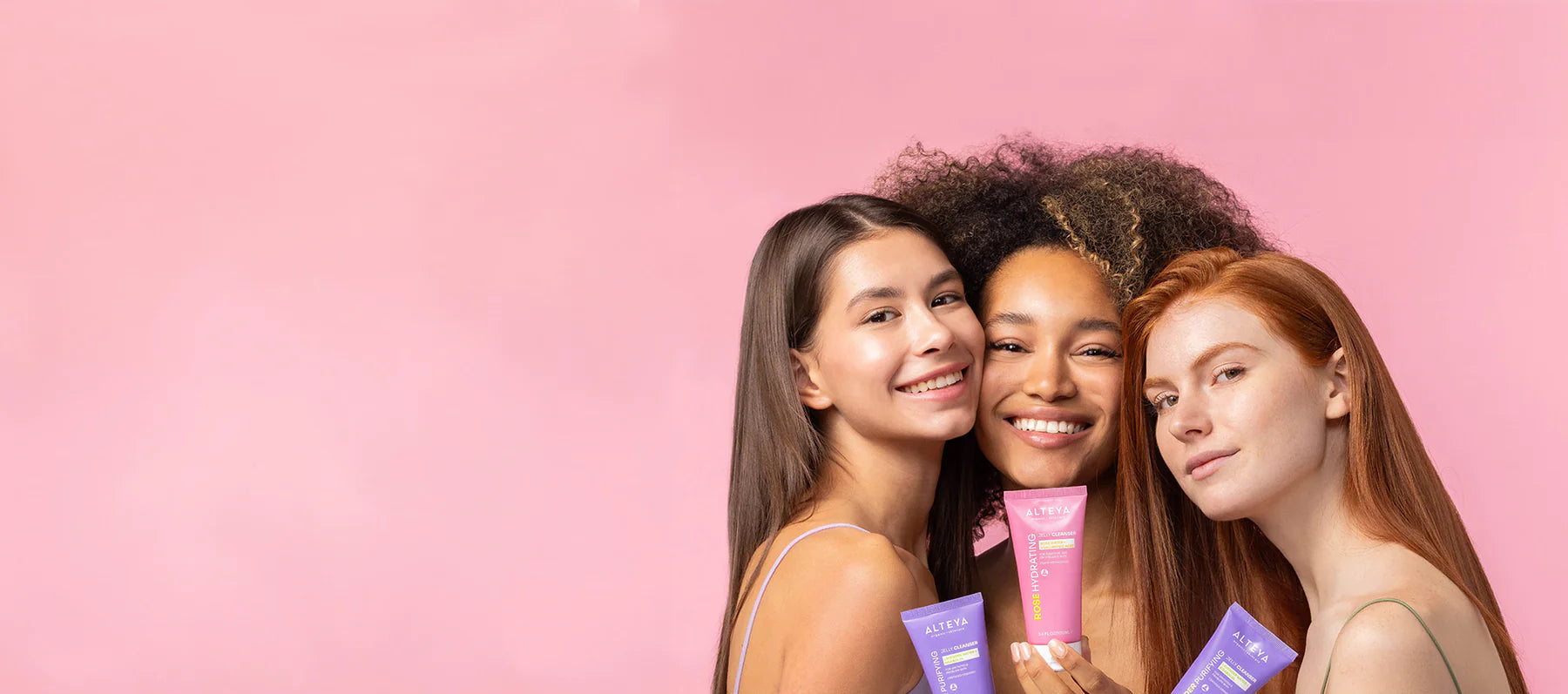Three young women are posing in front of a pink background.