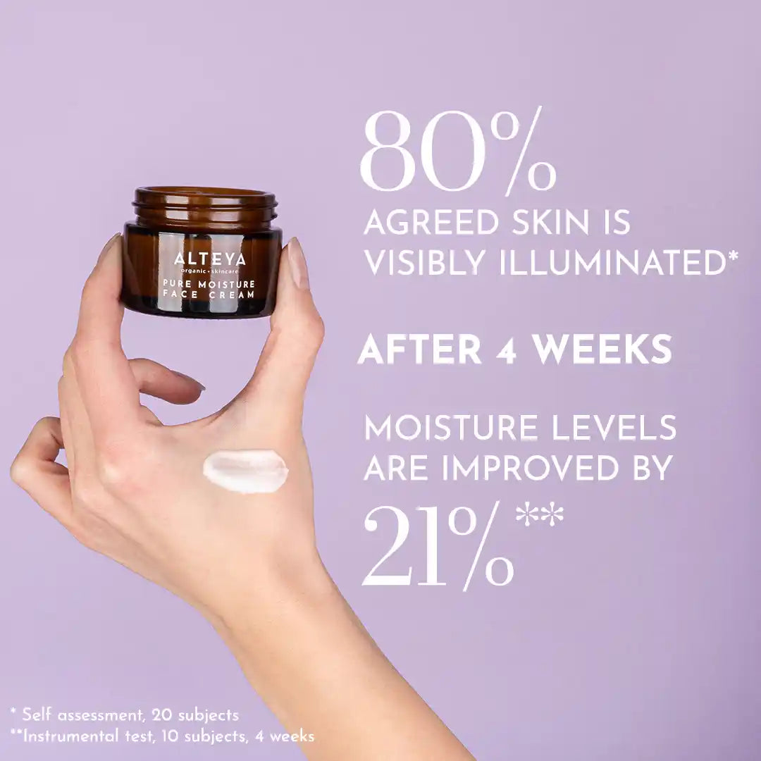 A hand holding a small jar of Pure Moisture Face Cream Luminous Rose against a purple background. Text on the image highlights product claims: "80% agreed skin is visibly illuminated" and "21% improved moisture levels". This brightening and hydrating formula offers exceptional anti-aging benefits.