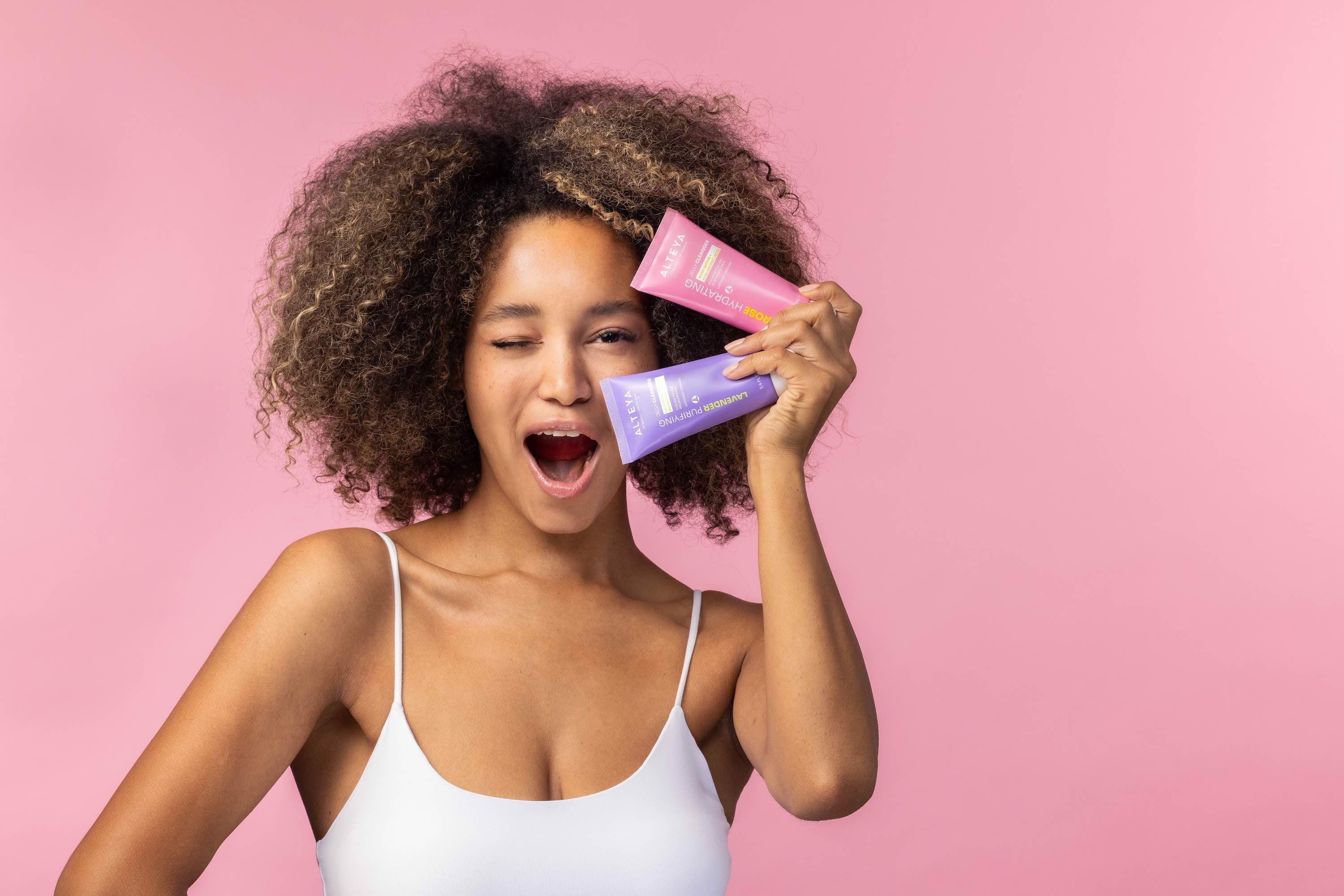 A young woman with afro hair is holding two tubes of skin care products.