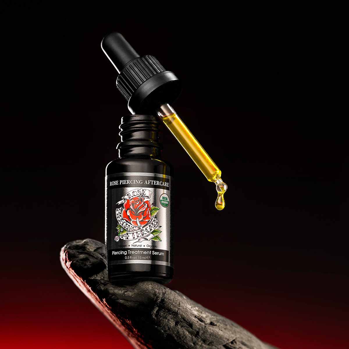 An organic bottle of Piercing Aftercare - USDA Certified Organic- 0.5 Fl Oz/15mL, a healing body piercing serum, sitting on top of a rock. (Brand Name: Alteya Organics)