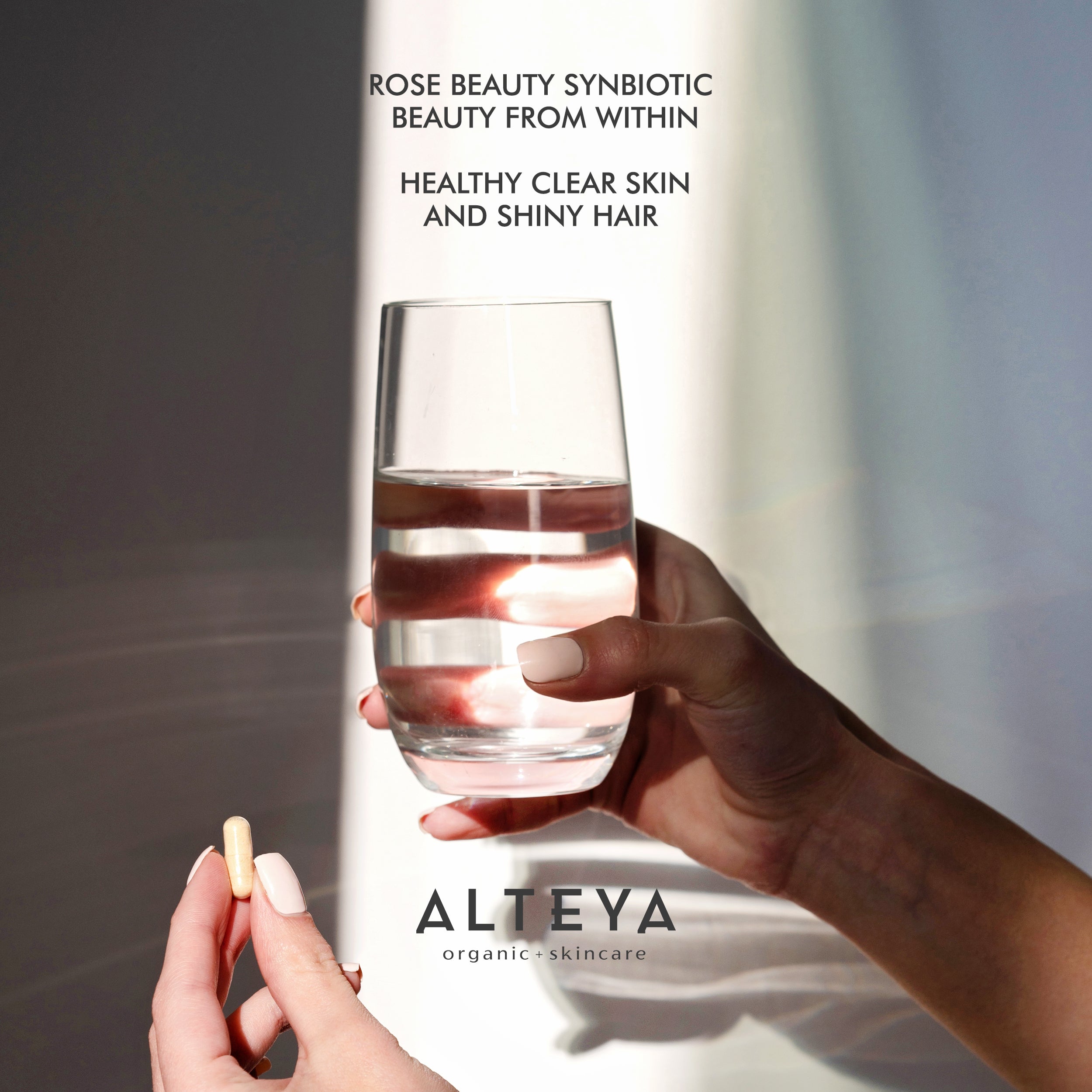A woman holding a glass of Alteya Organics' Rose Beauty Prebiotic and Probiotic - Synbiotic Skin & Metabolism Vegan Organic Supplement water.
