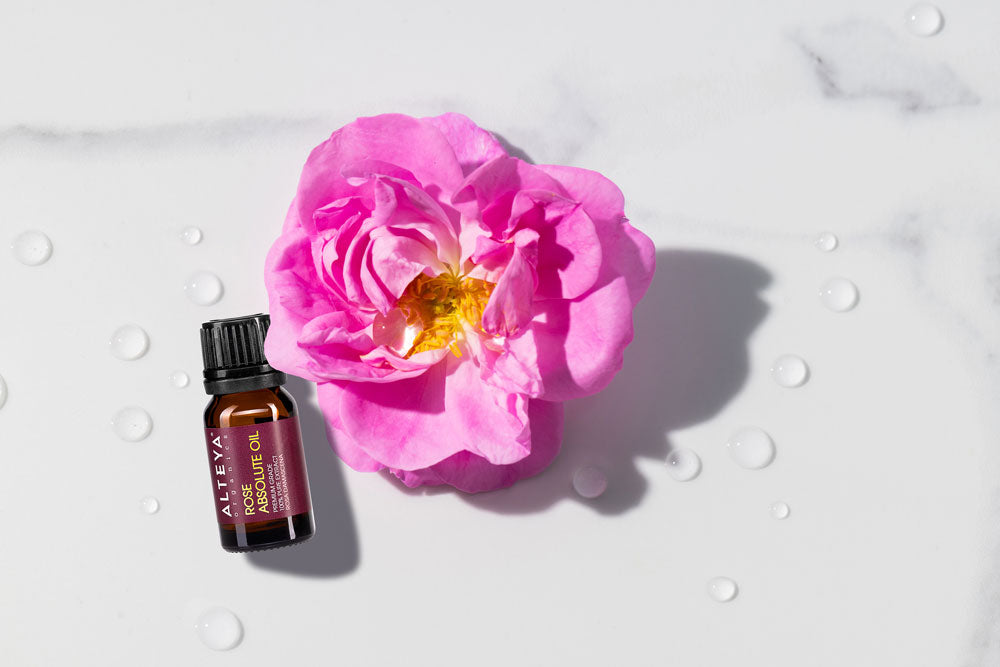 A bottle of rose essential oil next to a pink flower.