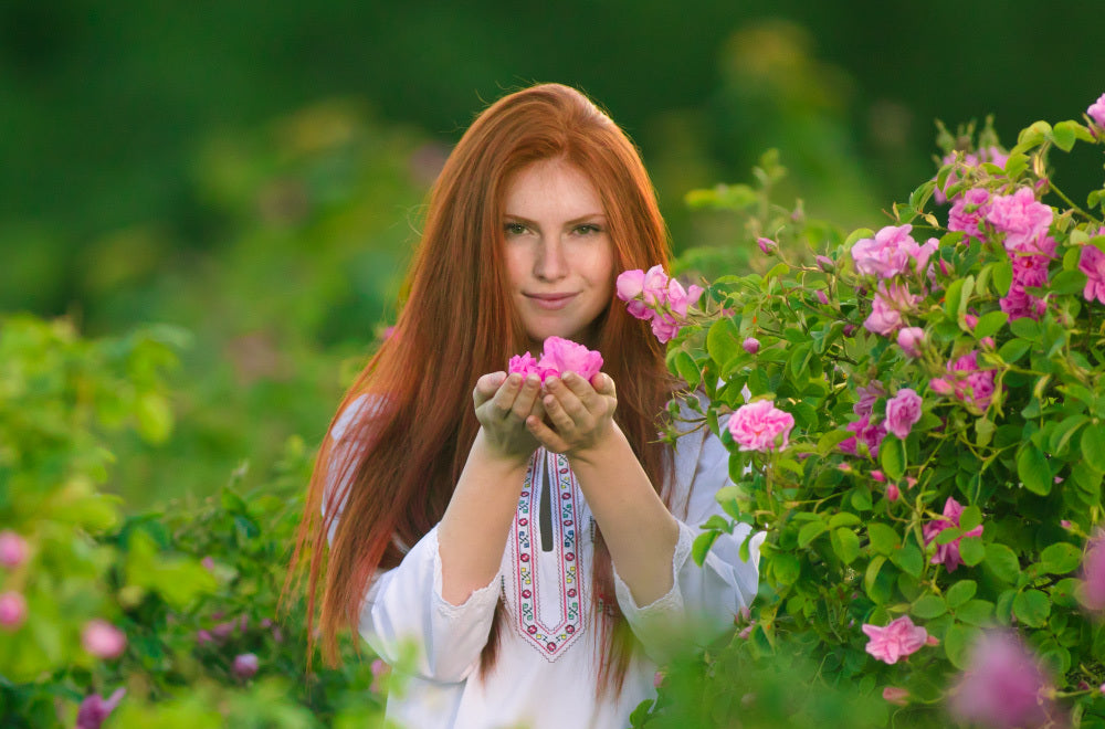 A woman with red hair is posing in a field of roses.